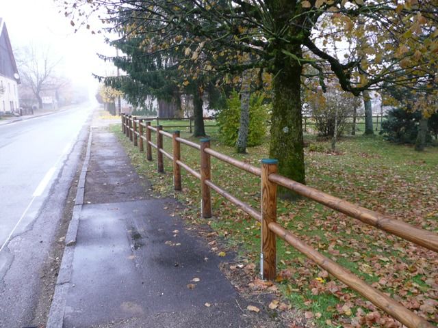 Clôture bois rond deux lisses longeant un trottoir de village, fabrication française SNMB — bois autoclave classe 4