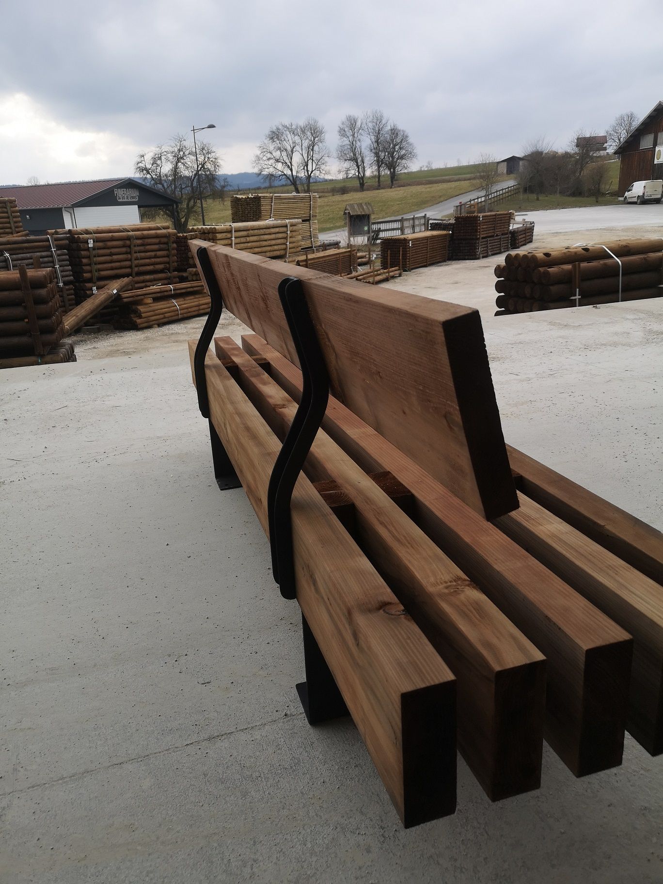 Vue arrière du banc premium en bois brun, dossier fixé par ferrures acier cintrées, parc à bois — fabrication française SNMB Menuiserie Bertin