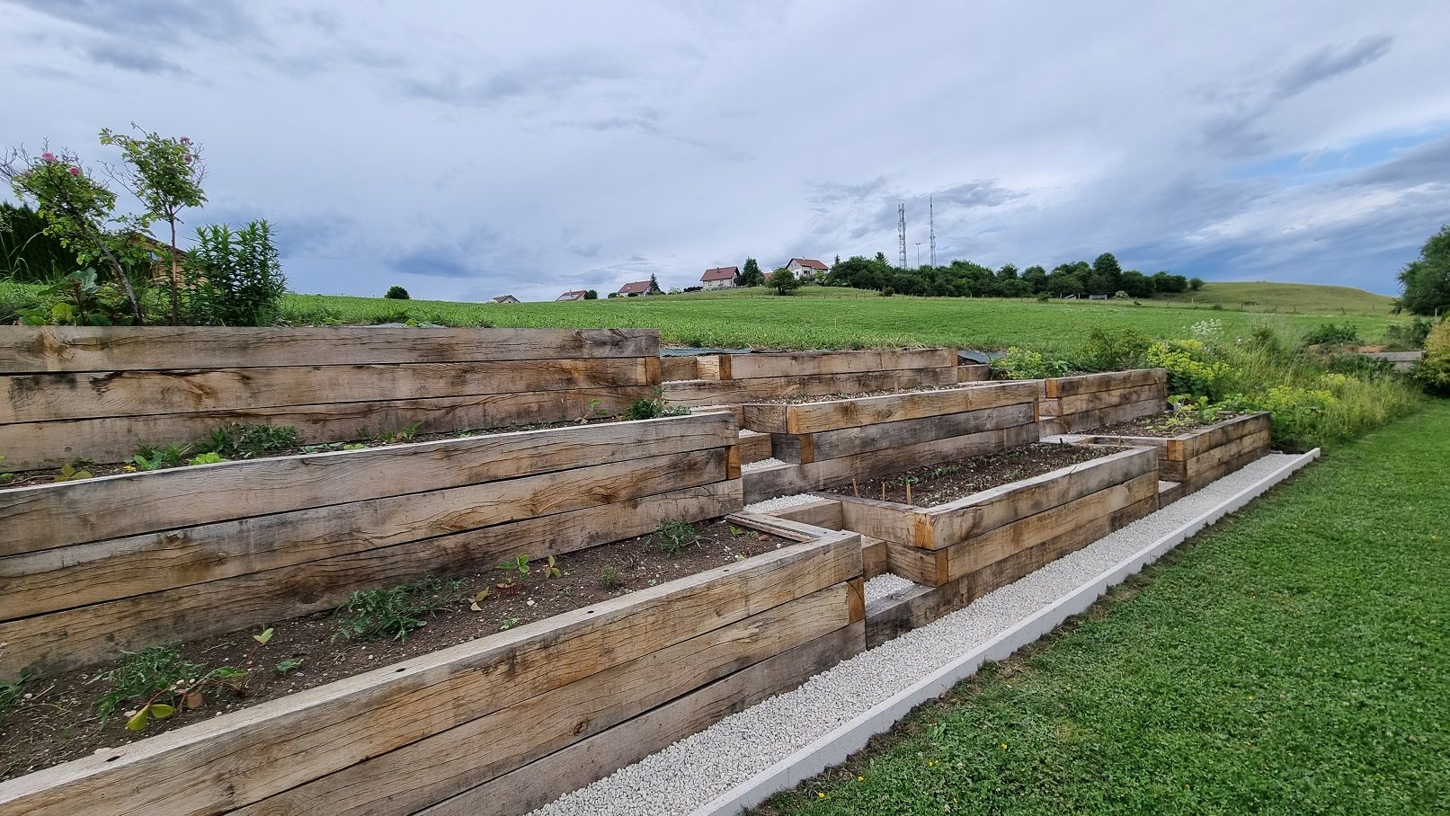 Chemin en gravillons blancs longeant la jardinière en pente en chêne — fabrication française SNMB Menuiserie Bertin